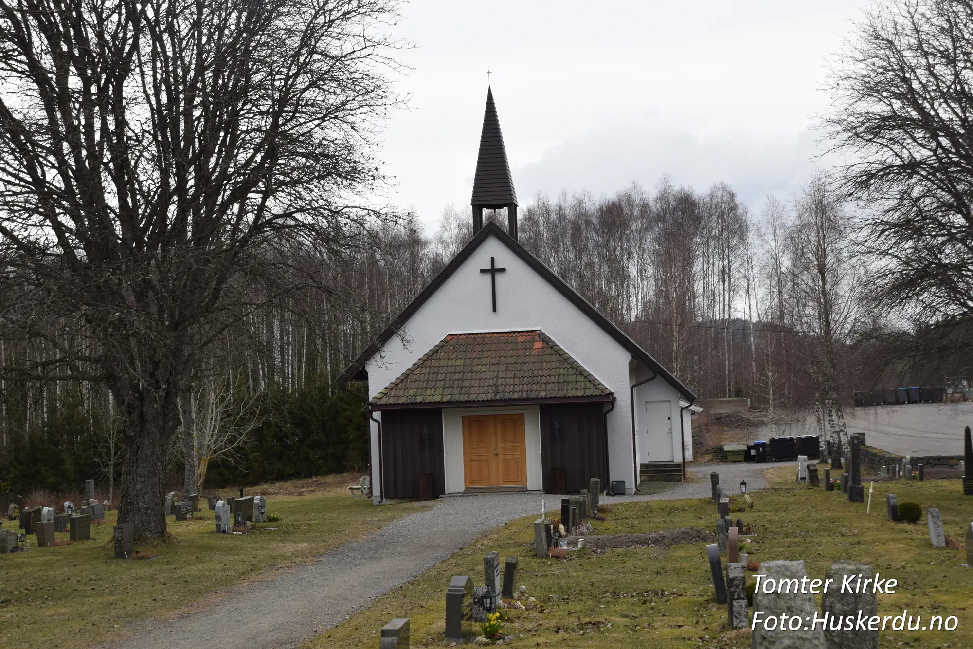 Tomter kirke, en tradisjonell langkirke i Indre Østfold, Østfold fylke, er bygget i tømmer og har en rik historie som strekker seg tilbake til 1600-tallet. Kirken er kjent for sin nygotiske altertavle fra 1880 og vakre kirkegård, som reflekterer områdets kulturarv. Foto: Huskerdu.no