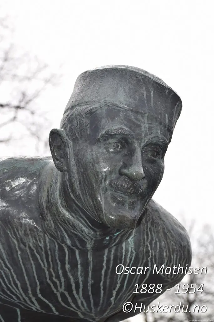 Oscar Mathisen – Skøytesportens ansikt i bronse Et nærbilde av statuen ved Frogner Stadion i Oslo, laget av Arne Durban i 1959. Oscar Mathisen, en av Norges største skøyteløpere, er udødeliggjort i dette kunstverket, som fanger hans fokus og lidenskap for sporten. Mathisen var kjent for sin utholdenhet og satte hele 14 verdensrekorder i løpet av sin karriere. Foto: Huskerdu.no