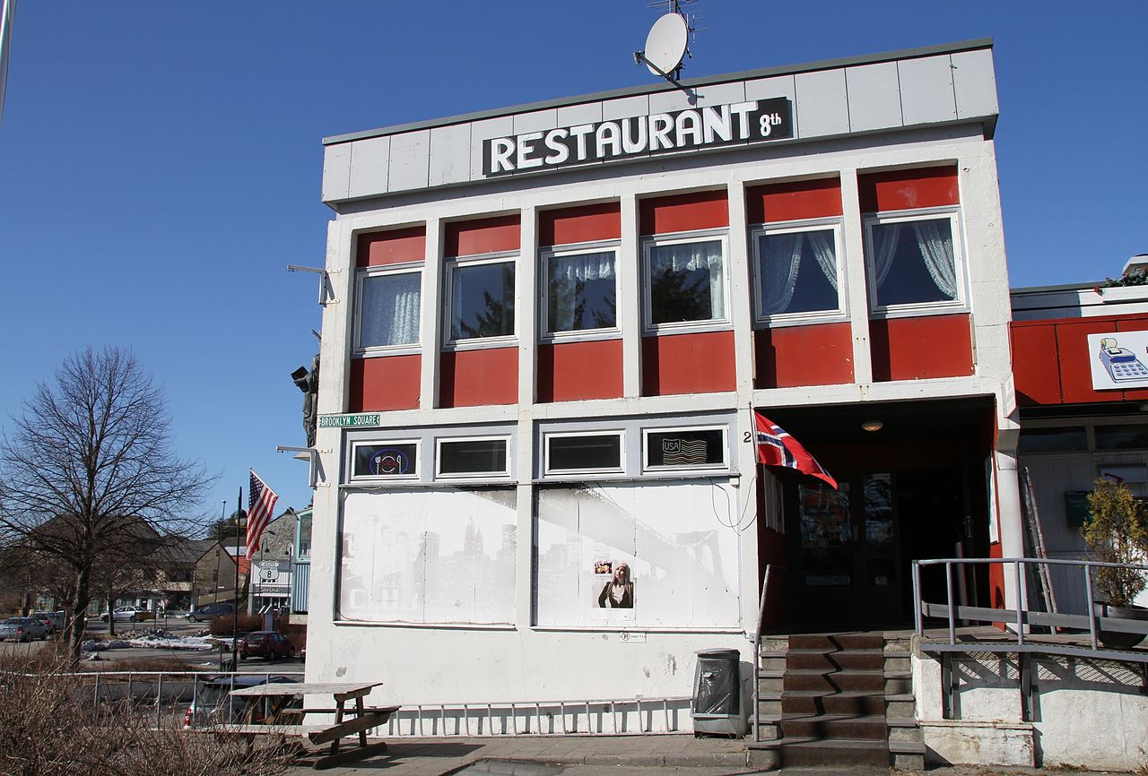 🍔🇺🇸 8th Avenue Restaurant & Diner i Brooklyn Square 🇺🇸🍔 8th Avenue Restaurant & Diner i hjertet av Brooklyn Square, Vanse, er et ikonisk symbol på tettstedets sterke bånd til USA. Restauranten, tidligere kjent som Trunken, tilbyr en autentisk amerikansk matopplevelse med burgere, milkshakes og klassiske diner-retter. Med amerikanske og norske flagg vaiende utenfor, speiler stedet den unike norsk-amerikanske arven i Vanse. Brooklyn Square er en sjelden destinasjon hvor amerikansk kultur er en naturlig del av hverdagen – perfekt for alle som vil oppleve et lite stykke Amerika i Norge! Foto: Bjoertvedt, CC BY-SA 3.0 https://creativecommons.org/licenses/by-sa/3.0 https://commons.wikimedia.org/wiki/User:Bjoertvedt vanse-8th-avenue-diner-brooklyn-square 8th Avenue Restaurant & Diner – Amerikansk matglede i Vanse Vanse, 8th Avenue Diner, Brooklyn Square Vanse, Vanse Farsund, American Festival Vanse, norsk-amerikansk kultur, amerikansk diner i Norge, norsk-amerikanske tradisjoner, USA i Norge, emigrasjon til Amerika, Vanse severdigheter, Vanse attraksjoner, Vanse restaurant