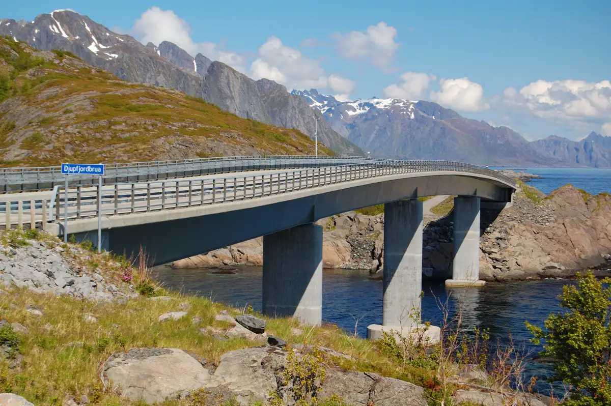 Djupfjordbrua i solskinn ☀️ Djupfjordbrua strekker seg elegant over fjorden i Moskenes kommune og binder sammen veien som snor seg langs Lofotens dramatiske kyst. Med høye fjell i bakgrunnen og havet tett på er dette en markant del av veien sørover mot Reine og Å i Lofoten. Brua gjør det mulig å ferdes trygt og effektivt gjennom et landskap som ellers ville vært utilgjengelig. Foto: Petr Šmerkl, CC BY-SA 3.0 commons.wikimedia.org/wiki/File:Djupfjord_Bridge_2009.JPG djupfjordbrua-i-lofoten-midt-i-fjellene Djupfjordbrua – Broforbindelsen gjennom Moskenes djupfjordbrua, djupfjord, moskenes, lofoten, bro, bru, fjell, kystvei Moskenes kommune