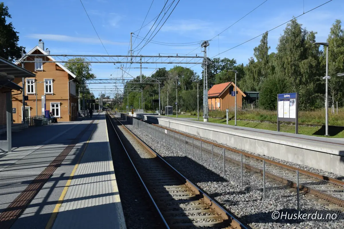 Spydeberg stasjon og Stasjonskafeen 🚉 Rett ved jernbanesporet ligger Spydeberg stasjon, et lite trehus som gir tettstedet et historisk preg. I bygget finner du Stasjonskafeen, et hyggelig sted å ta en pause mens du venter på toget eller vil møte lokalt folk. Stasjonen har vært et viktig knutepunkt på Østre linje i over hundre år og binder Spydeberg tett til både Oslo og Mysen. Foto: © Huskerdu.no Spydeberg stasjon og Stasjonskafeen – Foto: © Huskerdu.no spydeberg-sentrum-0007-04-09-2023-huskerdu Spydeberg stasjon og kafe – knutepunkt på Østre linje Spydeberg, Spydeberg stasjon, Stasjonskafeen, Østre linje, togstasjon Spydeberg, Indre Østfold