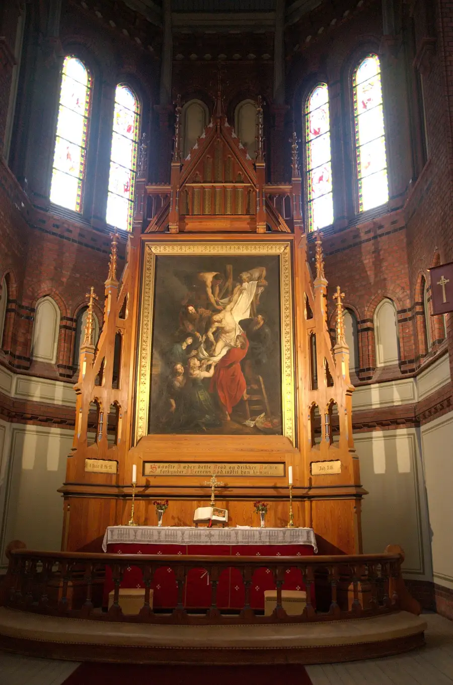 Alteret i Sagene kirke med maleri av Jesu nedtagelse fra korset omgitt av treskjæringer og glassmalerier.
