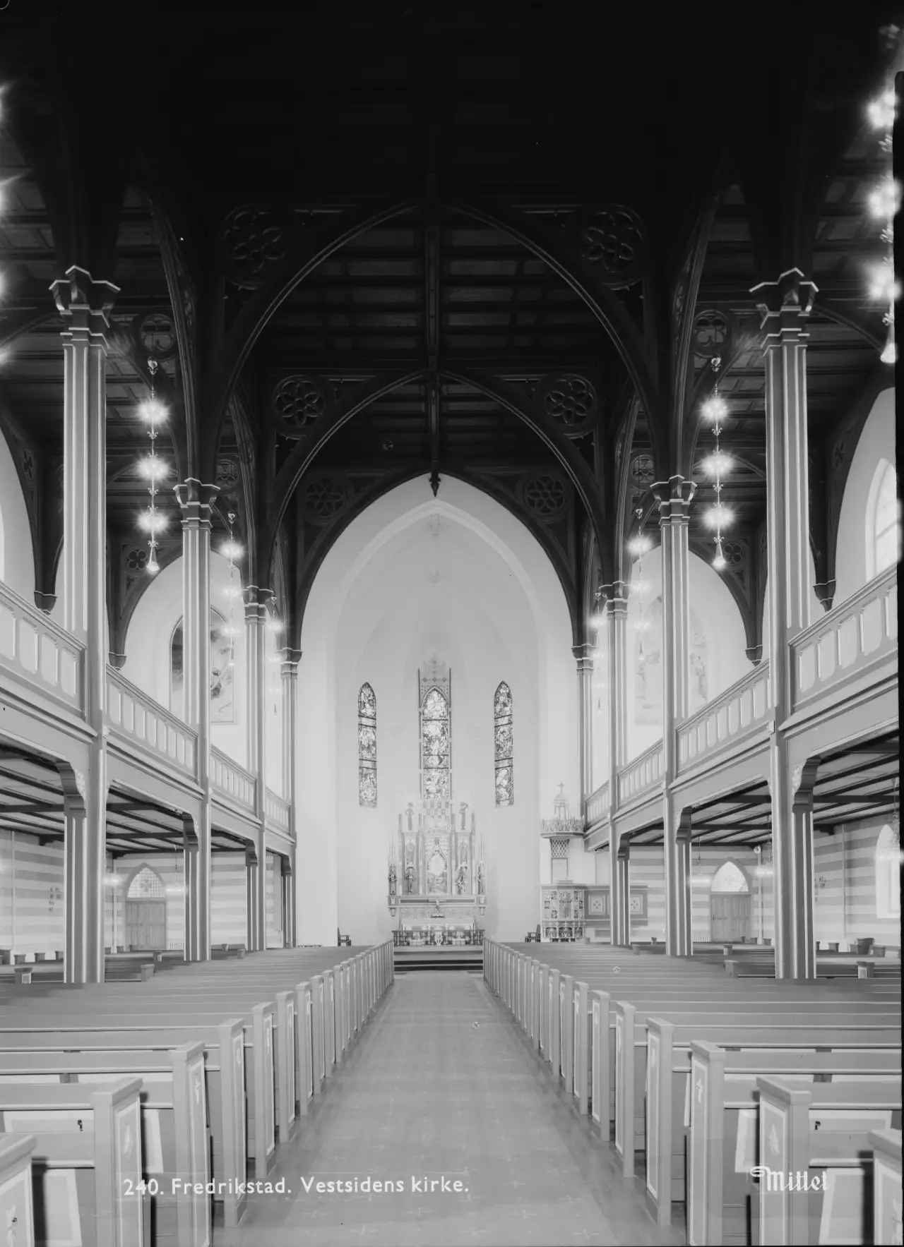 Interiøret i Fredrikstad domkirke fotografert i 1956 med utsikt mot alteret, glassmaleriene og søylerekkene i nygotisk stil, tatt av Jac Brun for Mittet & Co. AS.