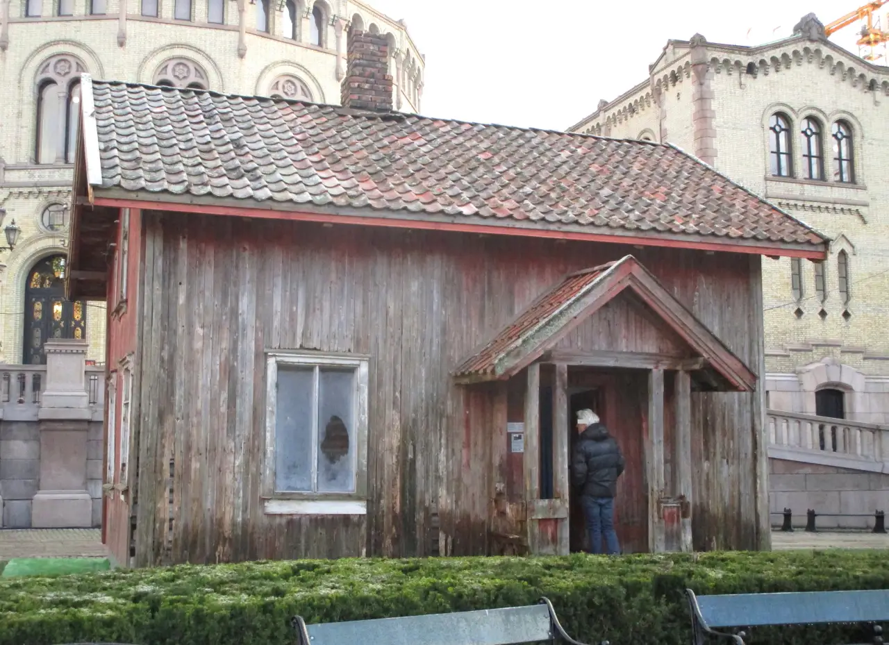 Vang-huset fra Hobøl gjenreist som kunstverket House of Commons foran Stortinget i Oslo i 2015, omgitt av de gule murbygningene på Eidsvolls plass.