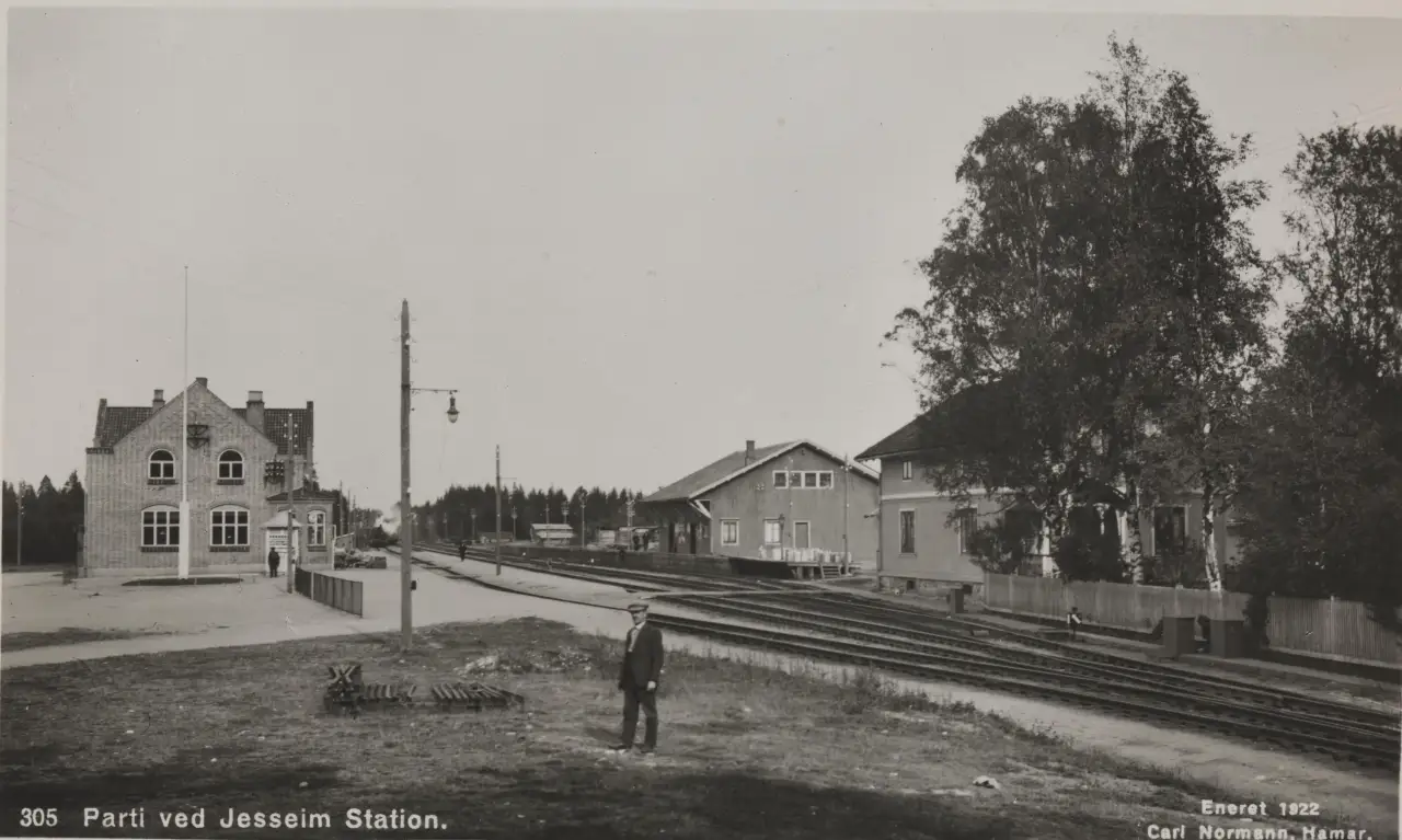 Jessheim stasjon rundt 1922, med murbygningen fra 1908 og en mann som står foran jernbanesporene.
