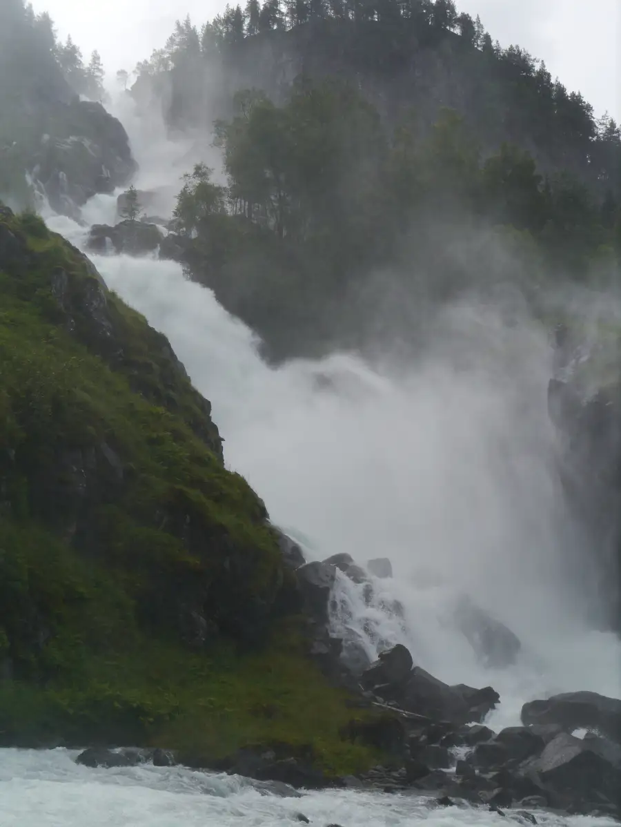 Låtefoss med høy vannføring 💦 Når vannføringen er på sitt kraftigste, fylles hele området rundt Låtefoss av fin vanntåke og dråper i lufta. Lyden fra fossen høres langt opp i fjellsidene, og de to fossearmene presser seg gjennom stein og skog før de møtes i et voldsomt fall mot dalbunnen. For besøkende langs riksvei 13 er dette et syn og en opplevelse man kjenner på kroppen. Foto: Zairon, CC BY-SA 3.0 https://creativecommons.org/licenses/by-sa/3.0/ https://commons.wikimedia.org/wiki/File:Hordaland_Laatefossen_6.JPG latefoss-hoy-vannforing-hardanger Låtefoss i høy vannføring – tåke og vannsprut over hele området latefoss, låtefoss, foss, hardanger, ullensvang, vannføring, riksvei 13, vestland Ullensvang kommune
