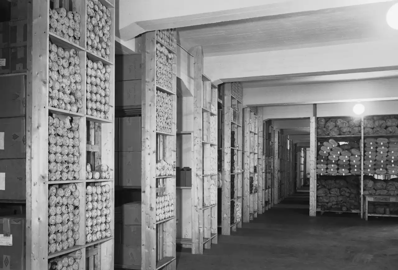 Råvarelageret ved Askim Gummivarefabrikk 📦 Råvarelageret var hjertet i fabrikkens forsyningssystem. Her ble alle innkjøp til produksjonen tatt imot, registrert og lagret – fra gummiballer og tekstilforsterkninger til kjemikalier brukt i vulkingen. Arbeiderne passet nøye på at beholdningen aldri gikk tom, for selv små forsinkelser kunne stoppe hele produksjonslinjen. Foto: Henriksen & Steen – Public Domain https://www.nb.no/lisens/#public-domain https://urn.nb.no/URN:NBN:no-nb_digifoto_20170926_00177_NB_HS_R_00115 ravarelageret-ved-askim-gummivarefabrikk-1942 Råvarelageret ved Askim Gummivarefabrikk 1942 askim gummivarefabrikk, askim gummivarefabrik, lager, ravarelager, industri, produksjon, gummi, ostfold industri Indre Østfold kommune