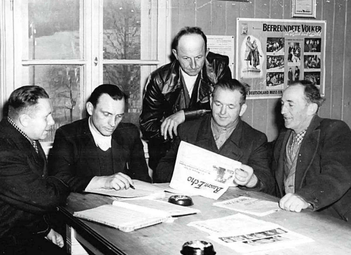 Menn sitter rundt et bord og leser avisen Bauernecho under et lokalt møte i DDR på 1950-tallet.