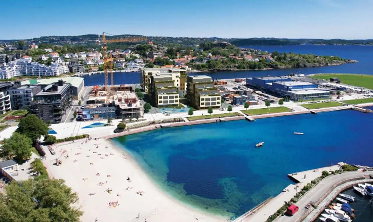 Bystranda i Kristiansand med langgrunn sandstrand, blått vann og utbygging rundt strandsonen sett fra luften.