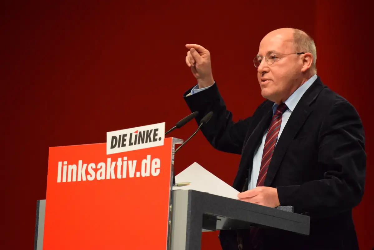 Gregor Gysi holder tale på et møte for Die Linke, med partiets logo foran talerstolen.