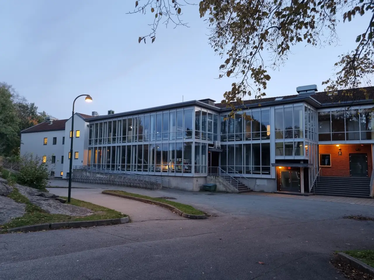 Grim skole sett fra nordsiden en stille kveld med lys fra klasserommene og glassfasaden som reflekterer himmelen.