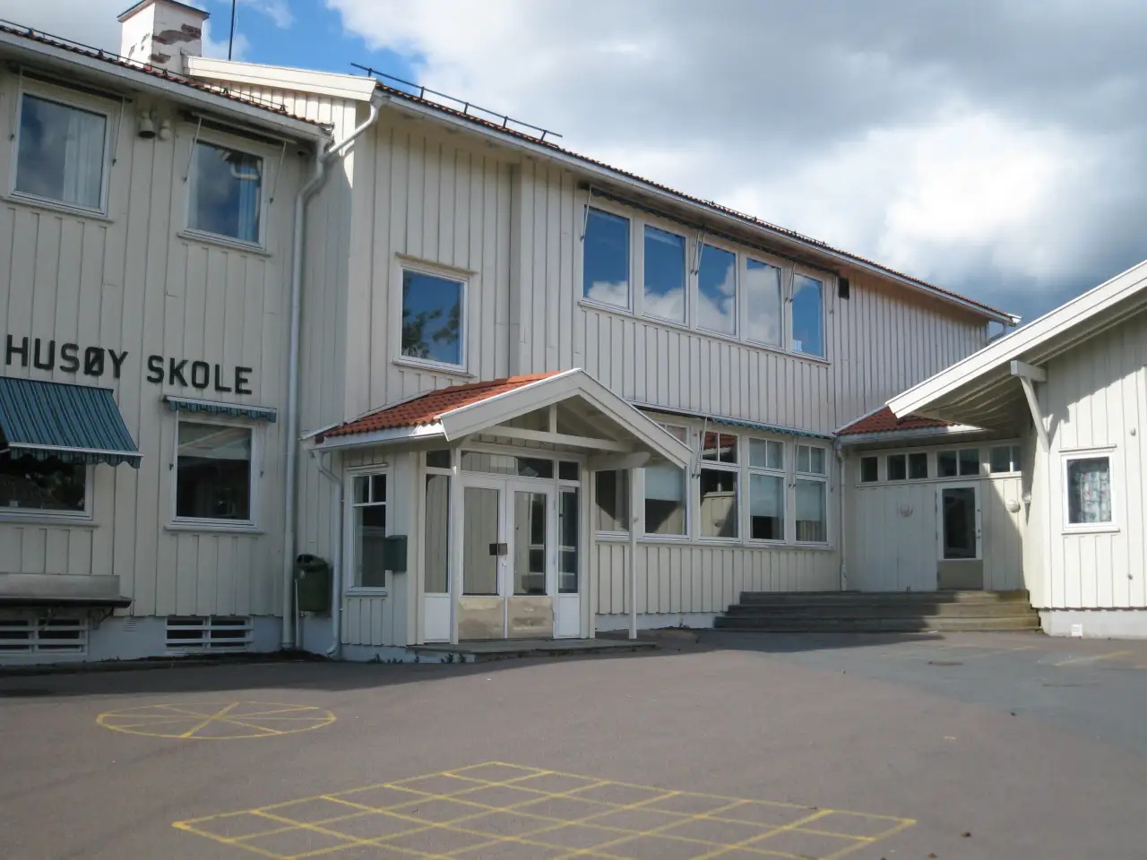 Inngangspartiet til Husøy skole med hvit trebygning og skolegård foran.