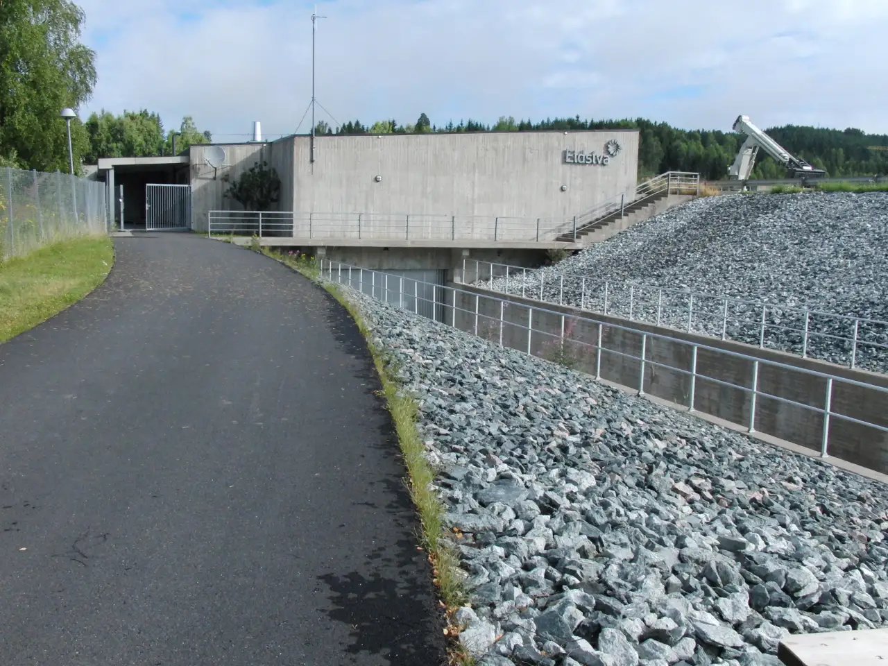 Kongsvinger kraftverk med steinlagt dam, betongbygg og turvei langs Glomma.