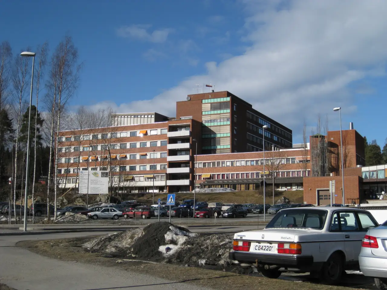 Kongsvinger sykehus med mursteinsfasade og parkeringsplass foran en klar vårdag.
