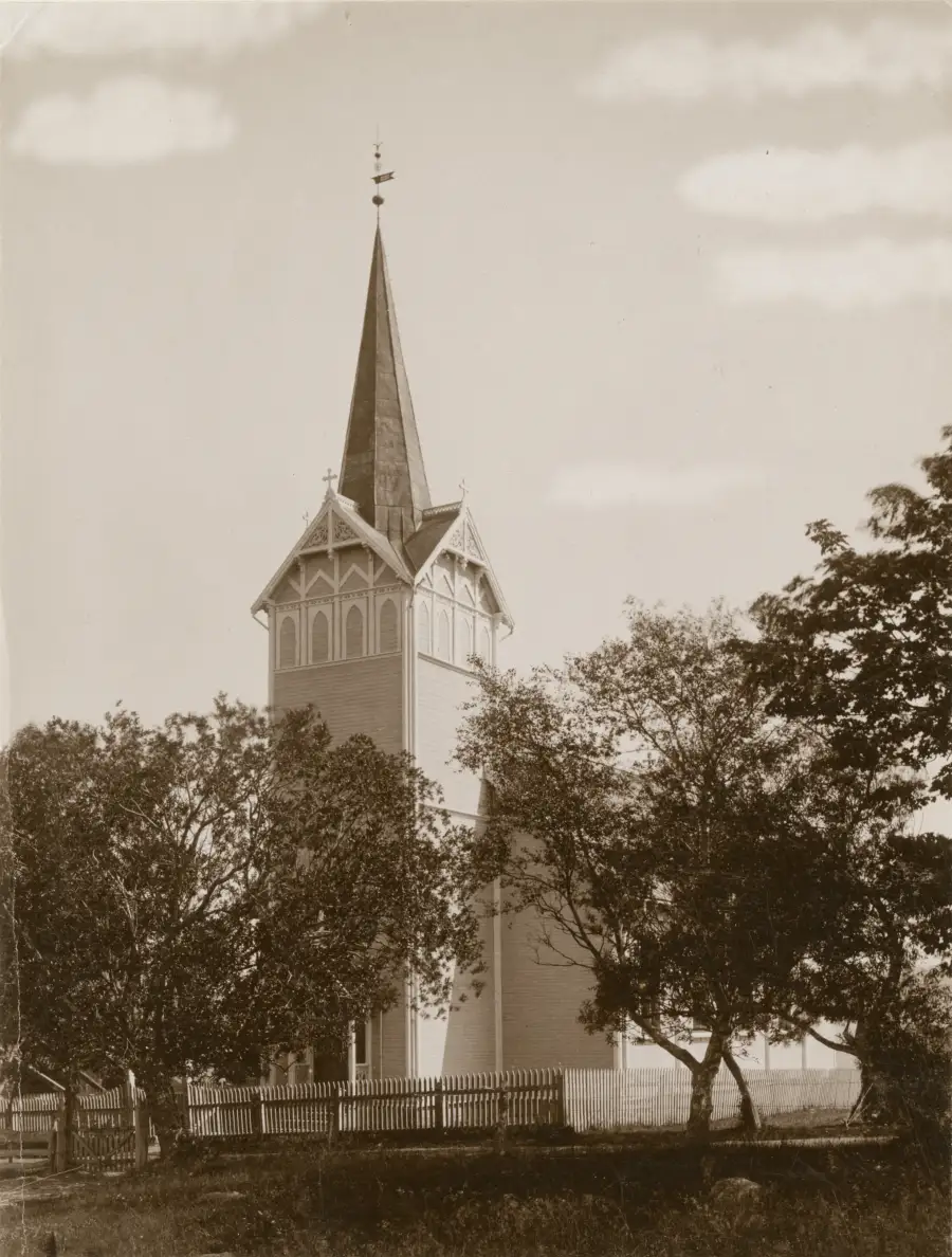Kvernes nye kirke med høyt spir sett bak trær på kirkegården.