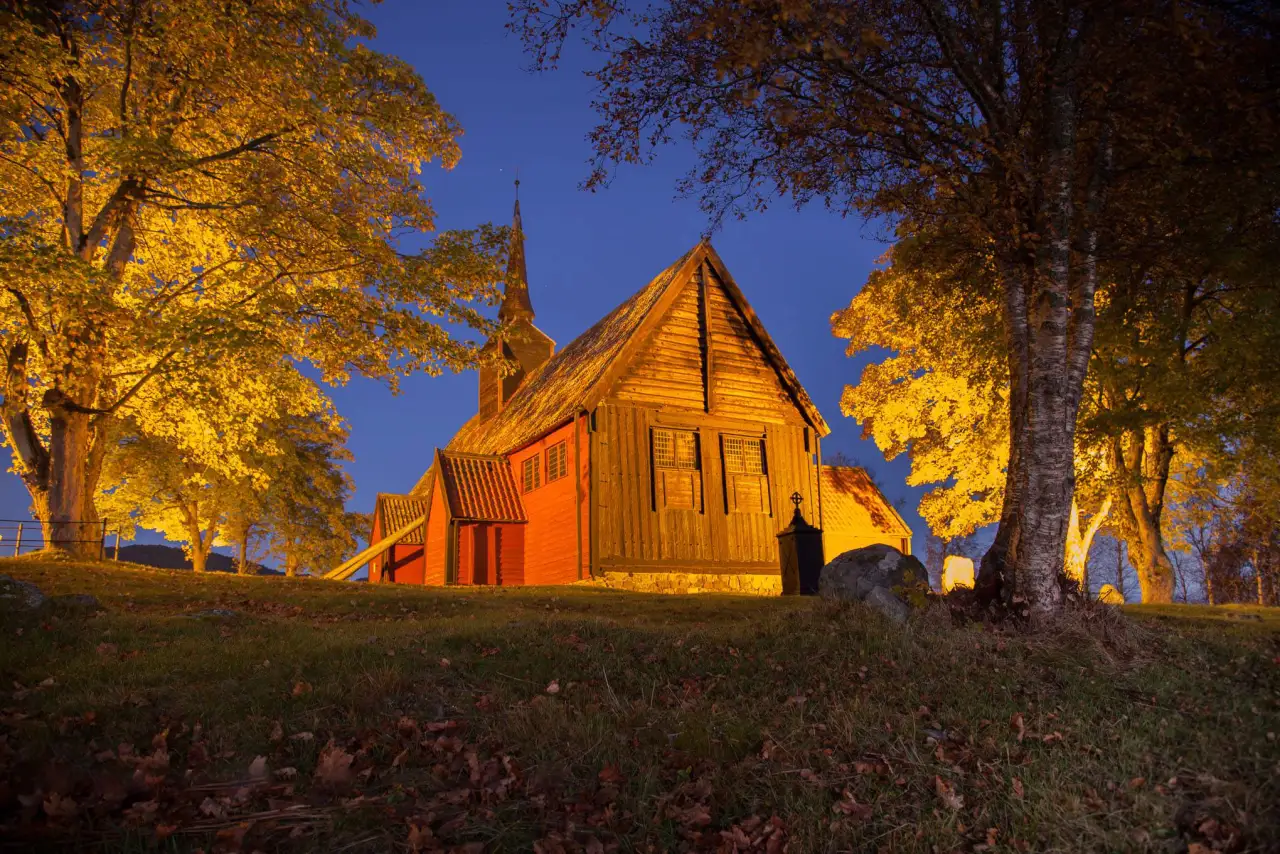 Kvernes stavkirke opplyst i høstlys med trær og gravplass rundt på Averøya.