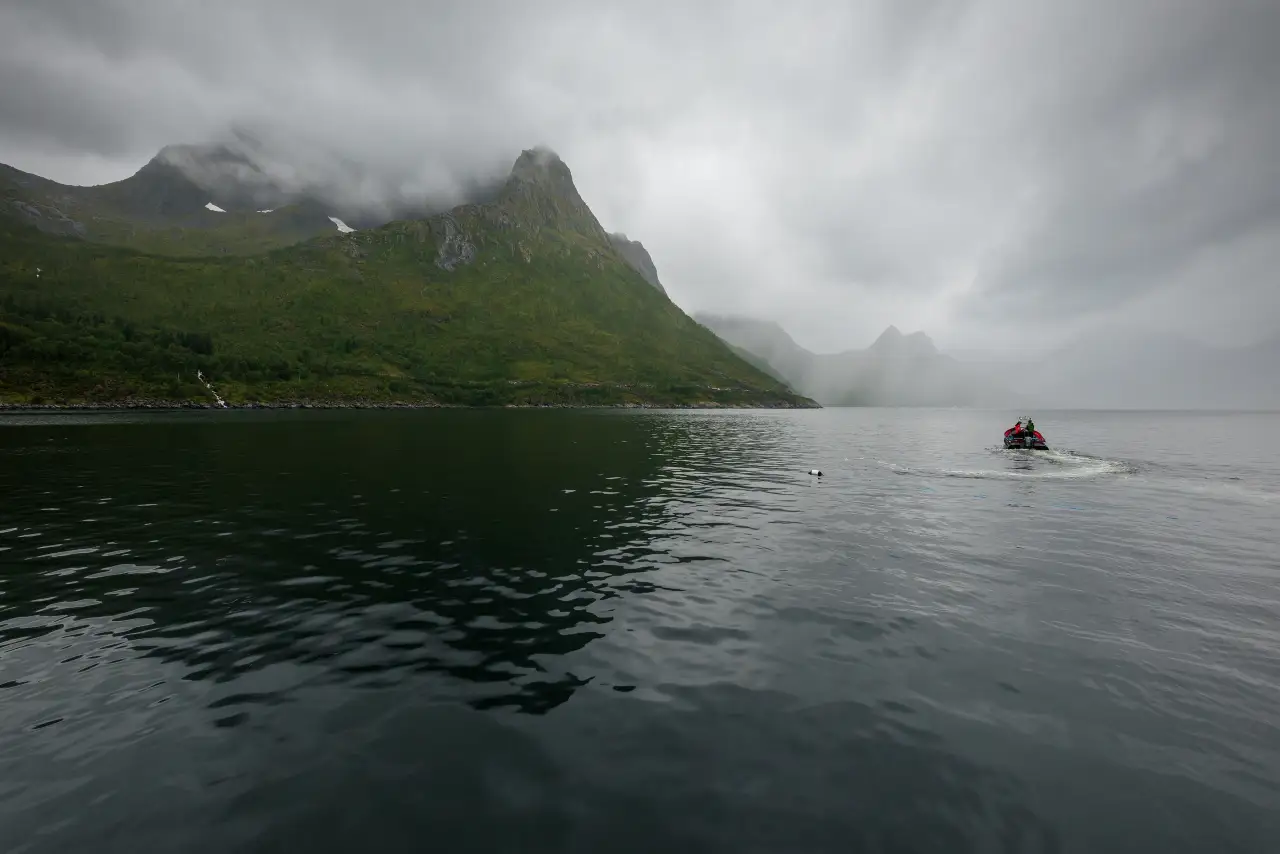 Mefjordbotn i regnvær med lave skyer over fjellene og en liten båt ute på fjorden.