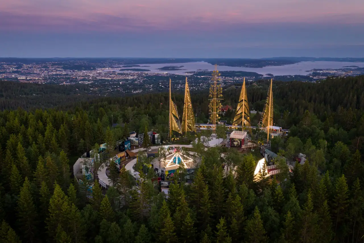 Roseslottet på Holmenkollen med opplyste installasjoner og utsikt over Oslo og fjorden i kveldlys.