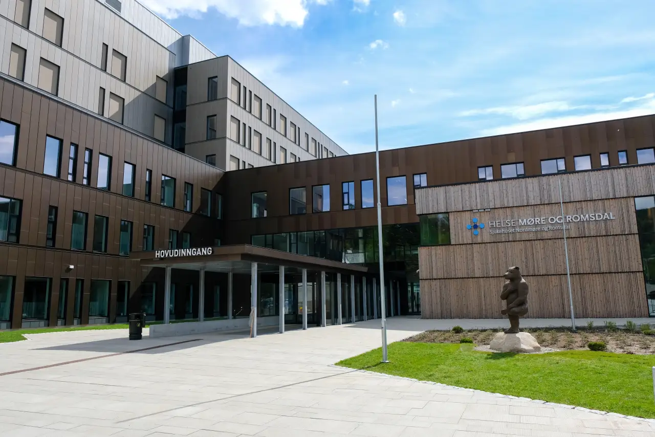 SNR Hjelset sin hovedinngang sett fra plassen foran bygget med tre og metall i fasaden.