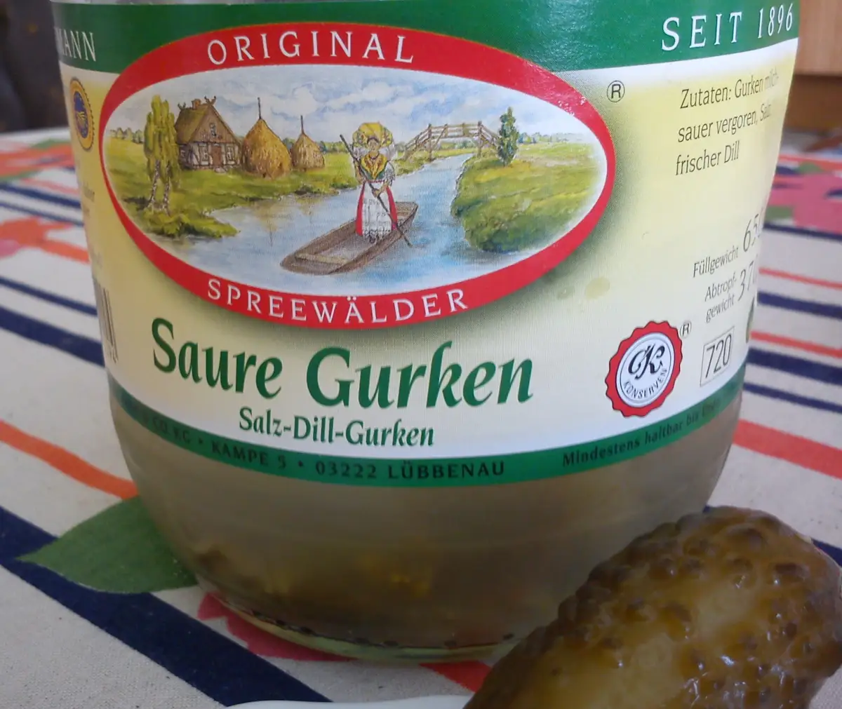 Nærbilde av et glass med Spreewaldgurker fra Tyskland, med en agurk ved siden av.