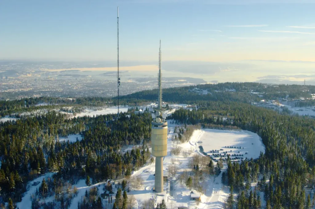 Tryvannshøgda med Tryvannstårnet og senderantenne omgitt av vinterkledd skog og utsikt over Oslo og fjorden.