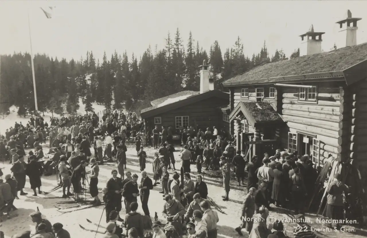 Tryvannstua i Nordmarka med tett folkeliv og skiløpere utenfor hytta en vinterdag på 1930-tallet.