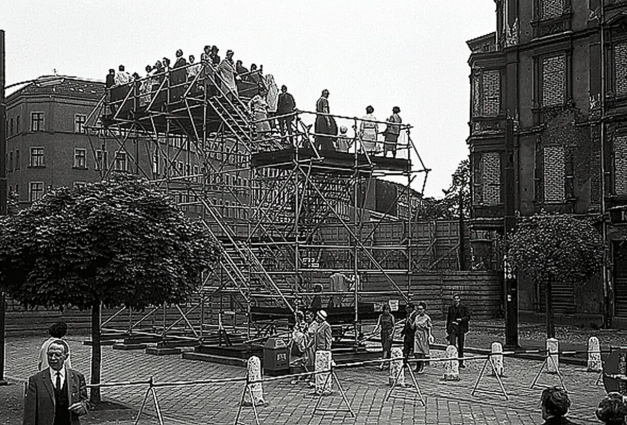 Folk står på en utsiktsplattform ved Bernauer Straße i West-Berlin for å se over Berlinmuren mot øst i 1965.