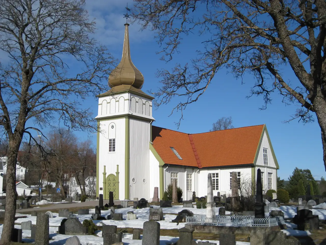 Vinger kirke med løkkuppel og kirkegård i forgrunn en klar vinterdag.