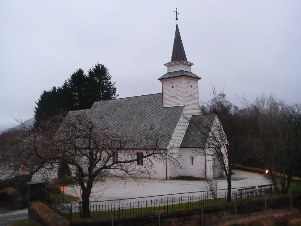Åsane gamle kirke på Saurås i Åsane bydel omgitt av trær og kirkegård.
