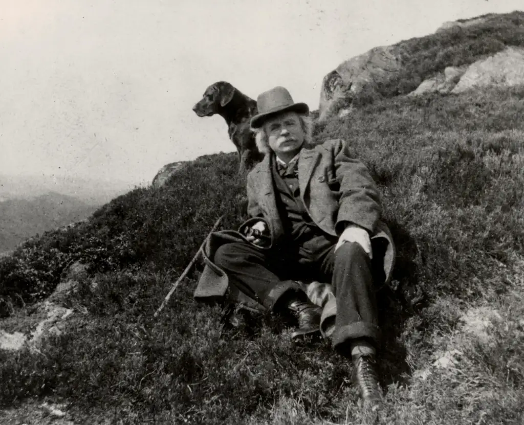 Edvard Grieg sitter i gresset på Løvstakken med hund ca. 1900.