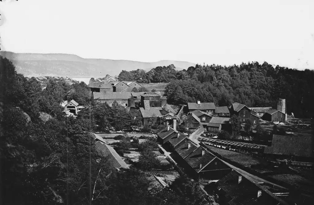 Eidsfoss industristed med tett trehusbebyggelse verk og skogkledde åser i bakgrunnen.