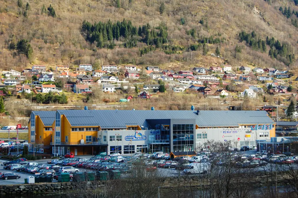 Øyrane Torg i Arna sentrum med parkeringsplassen i forgrunnen og boligbebyggelse i fjellsiden bak.
