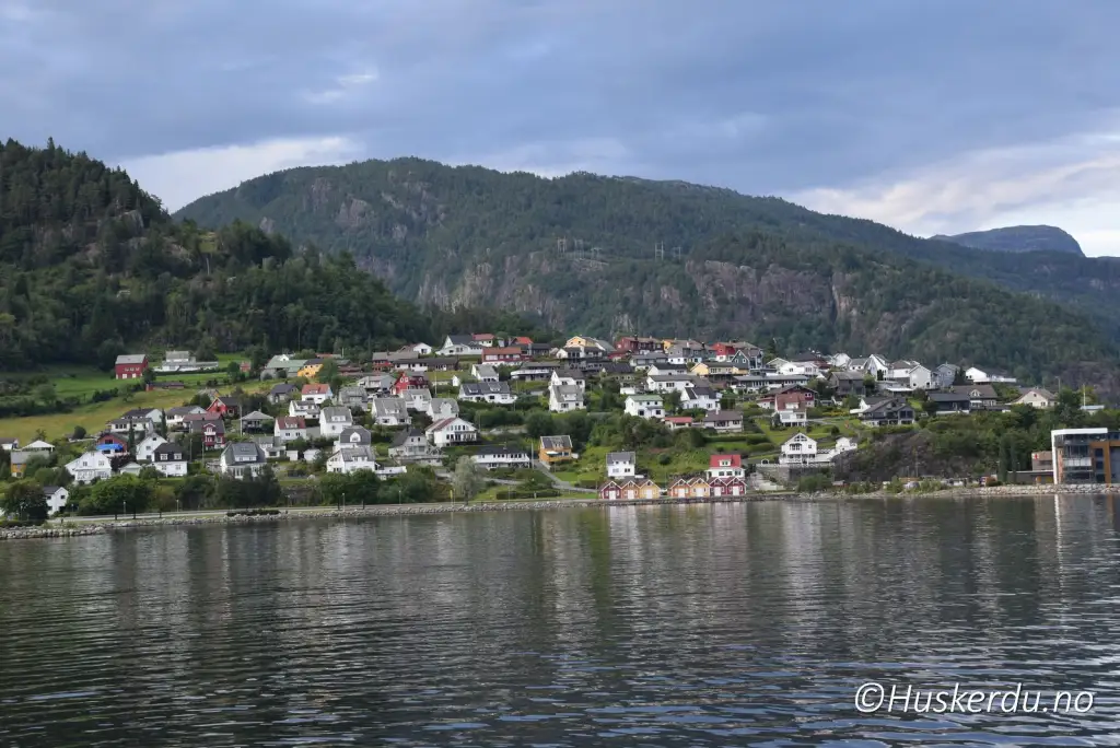 Sauda sentrum med bolighus langs Saudafjorden og bratte fjell i bakgrunnen