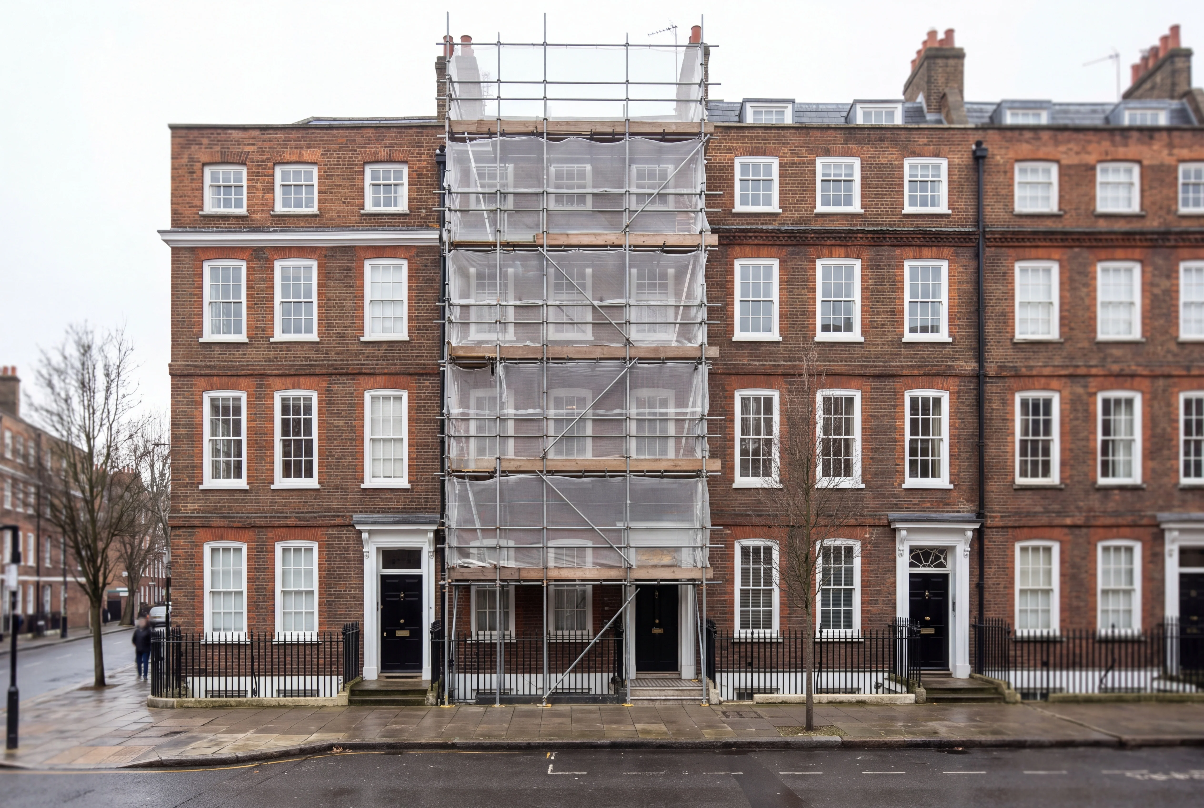 A row of Georgian brick townhouses with one facade covered in scaffolding and mesh