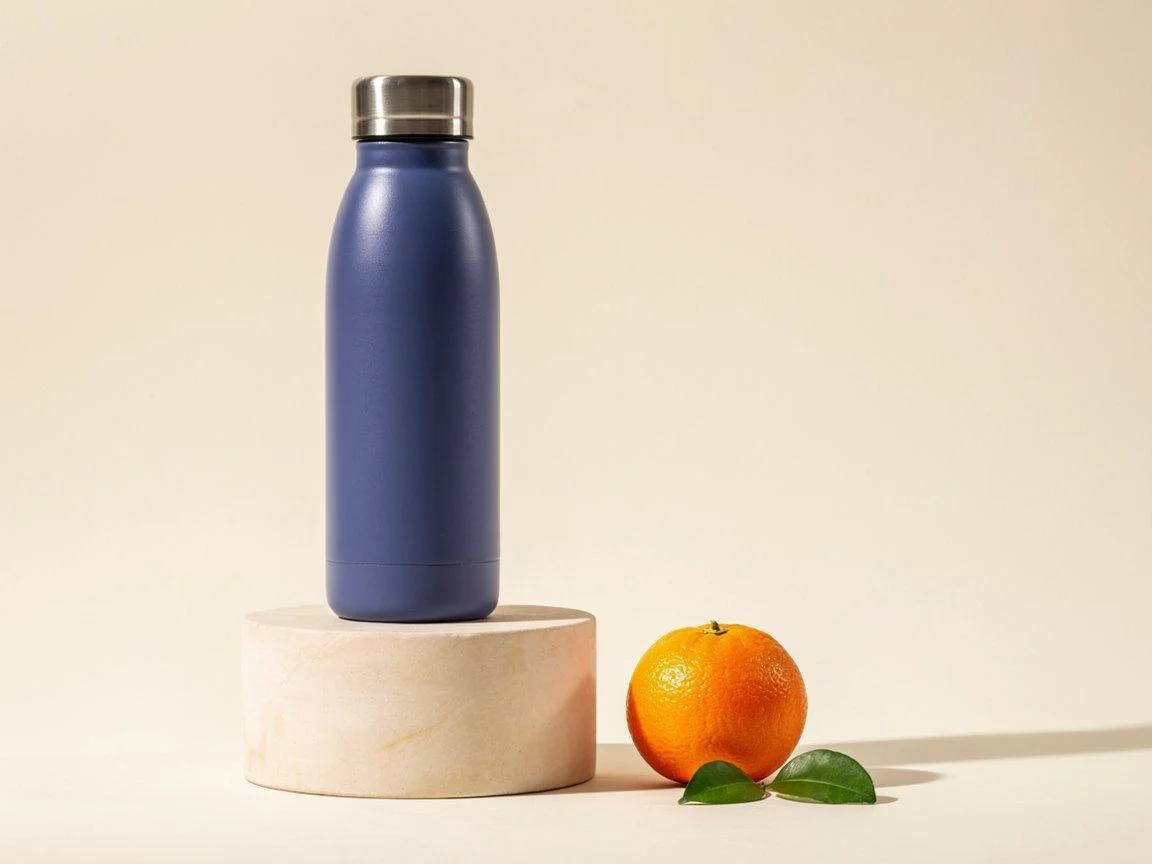 Ideogram product-image test showing a blue water bottle on a beige pedestal, with an orange and two leaves beside it and open space to the right.