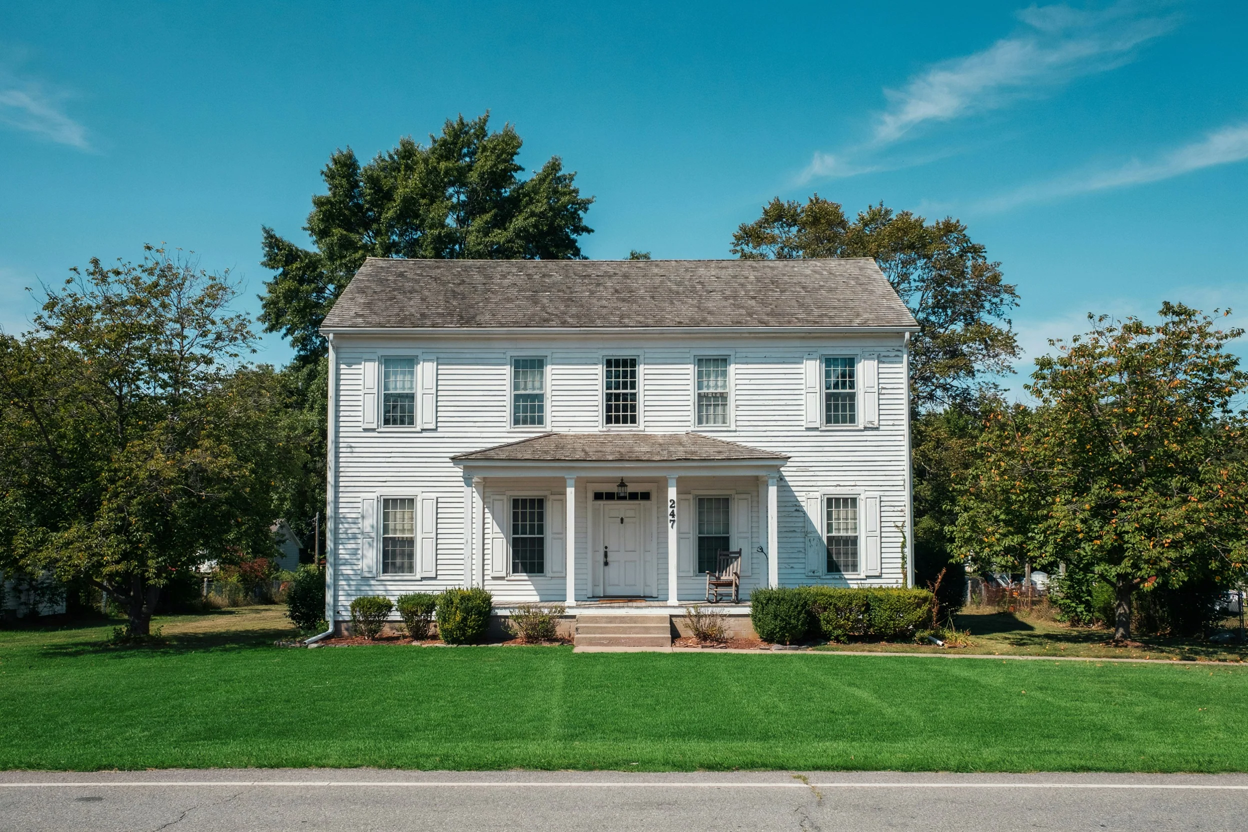 The same farmhouse with the whole front lawn lush, green, and freshly mowed