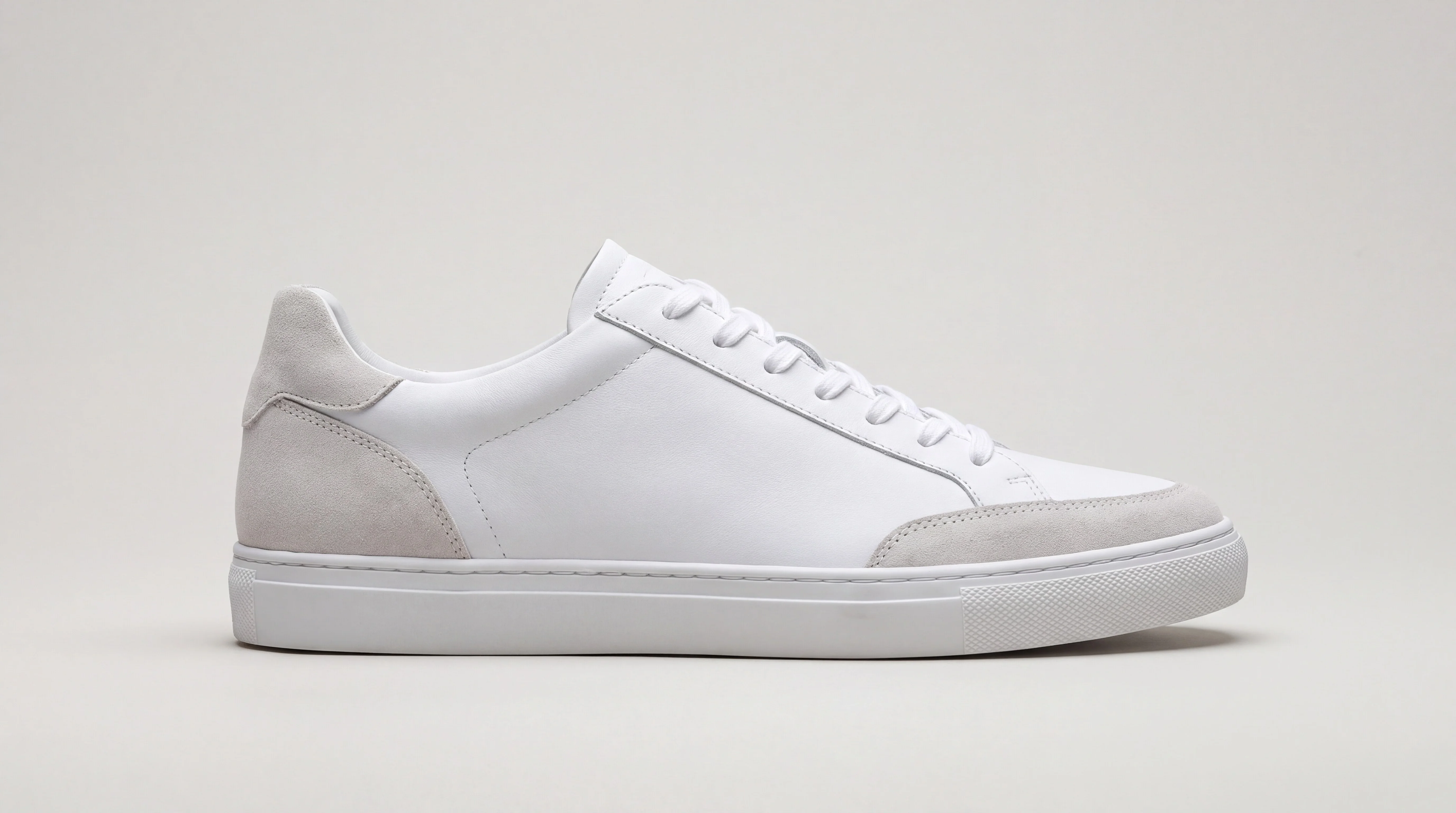A studio photo of a white sneaker with light gray suede panels