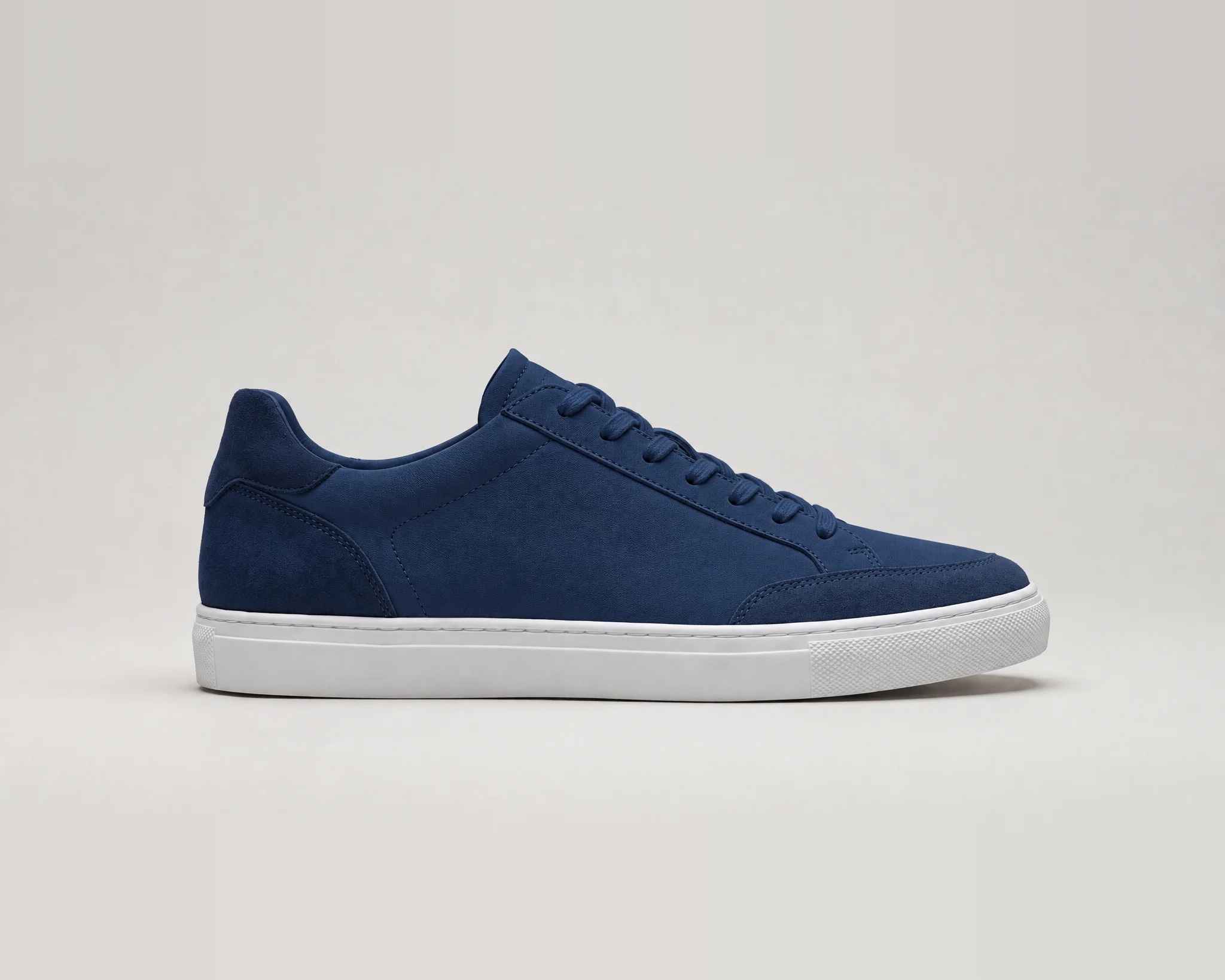 The same sneaker recolored navy. The upper, laces, heel panel, and toe cap are navy, the sole stays white, and the silhouette and stitched panel lines follow the original.