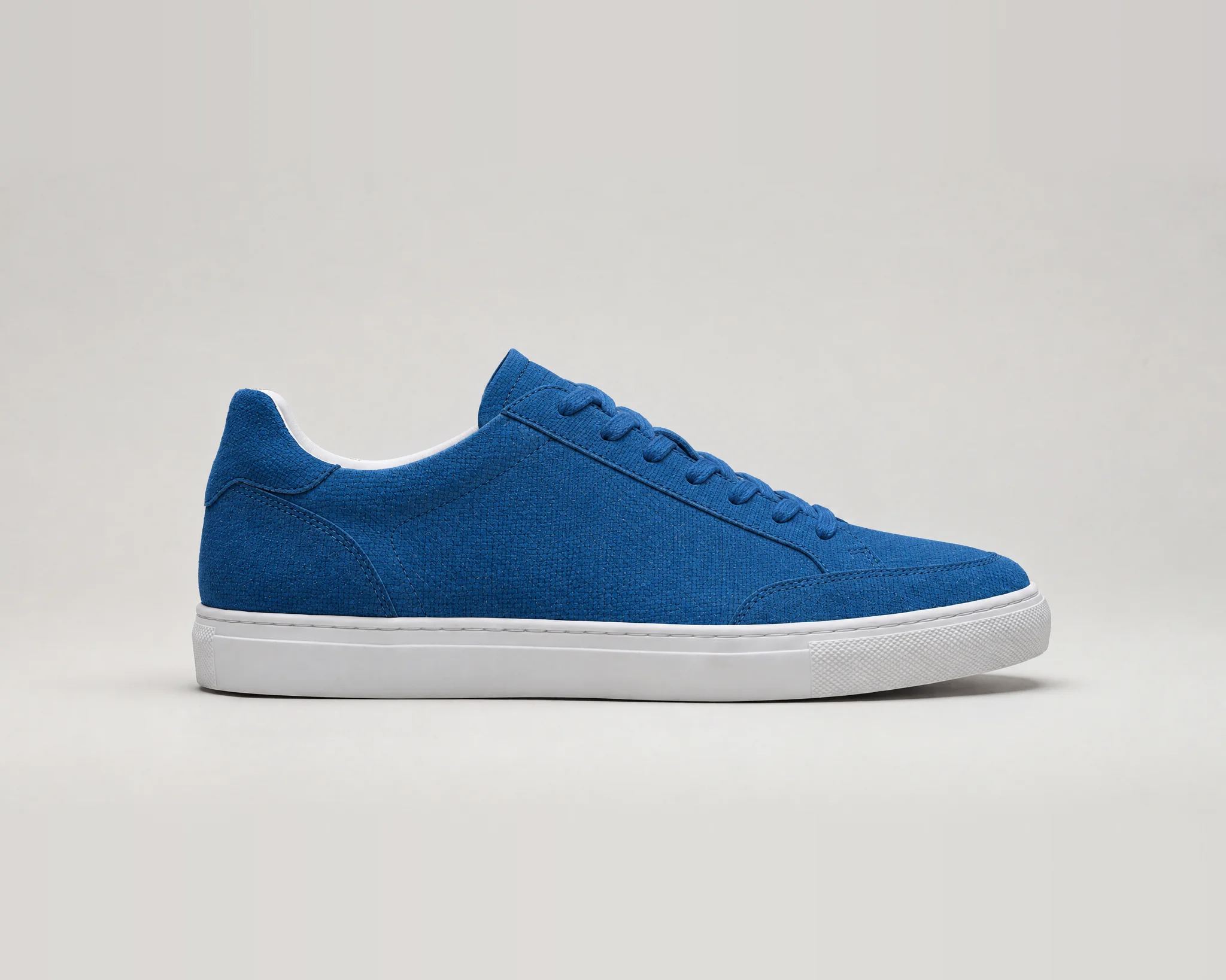 The same sneaker with its whole upper, including the heel panel and toe cap, re-rendered in blue woven canvas. The laces are blue, and the sole and lining stay white.