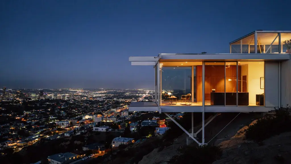 Julius Shulman-style architectural photograph: mid-century modern glass house cantilevered over a hillside at dusk, warm amber interior, city lights below.
