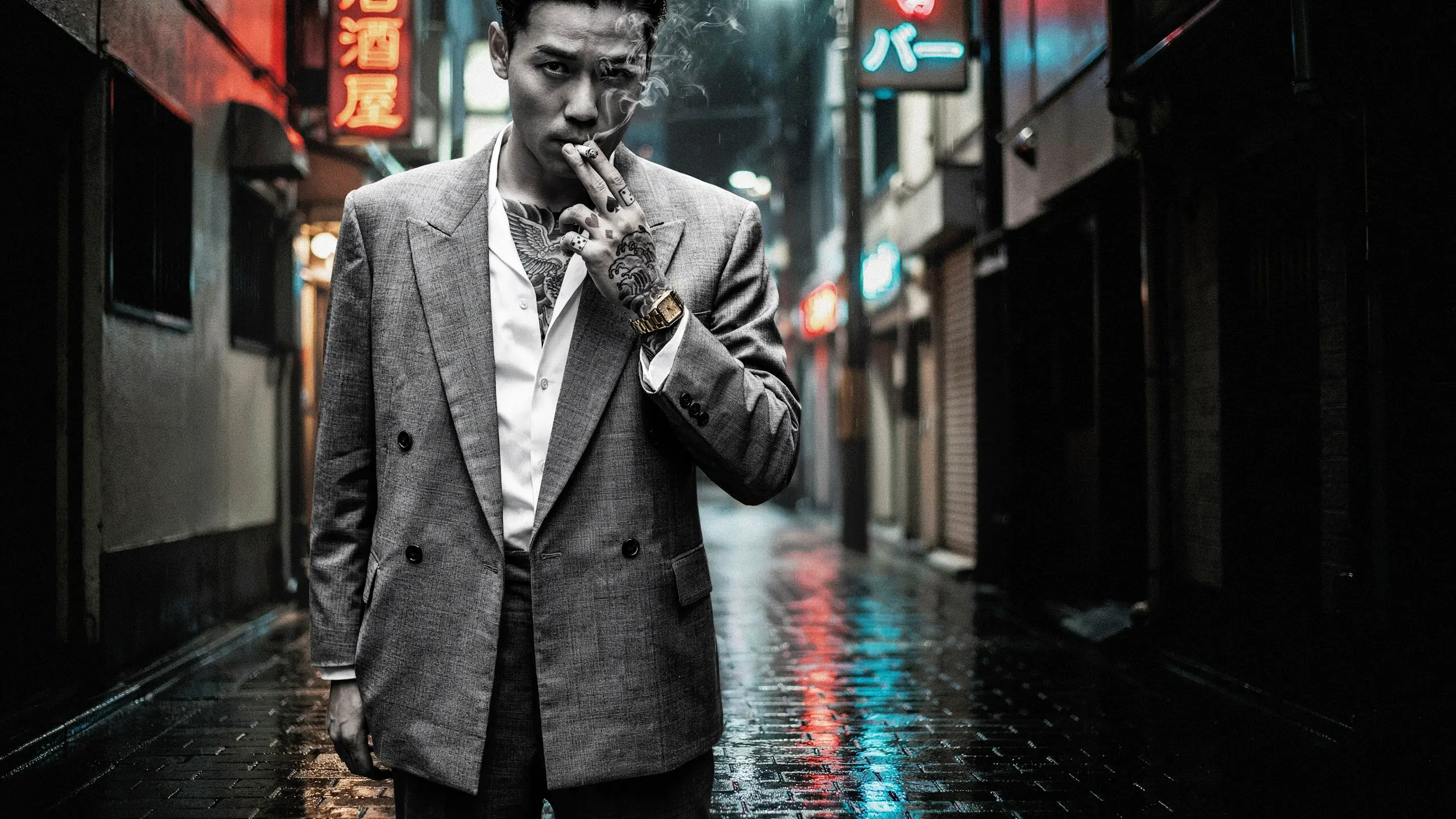Tattooed man in a sharkskin suit holding a cigarette, Shinjuku back-alley at night, high-contrast black-and-white, wet cobblestones, neon bokeh.