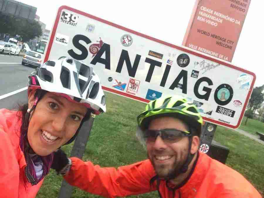 Dos jóvenes adultos posan en frente de un cartel de la carretera que pone "Santiago"