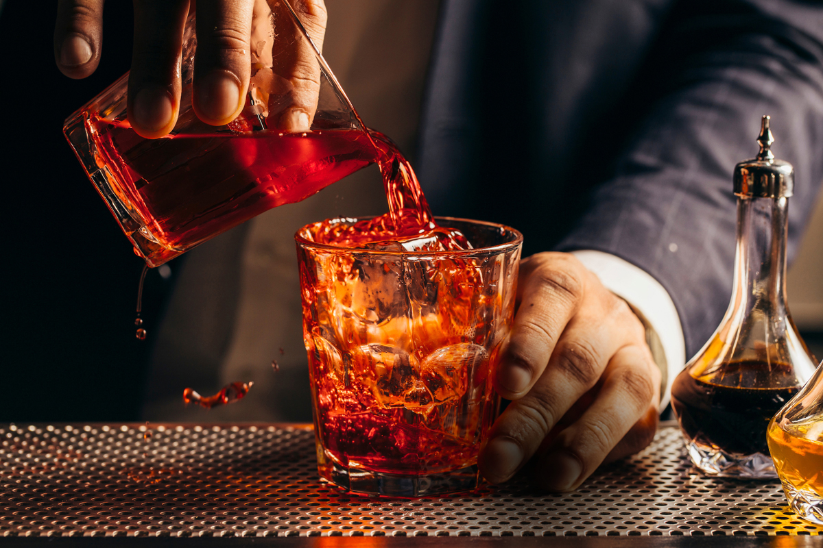 close up photo of a negroni cocktail being poured into a glass