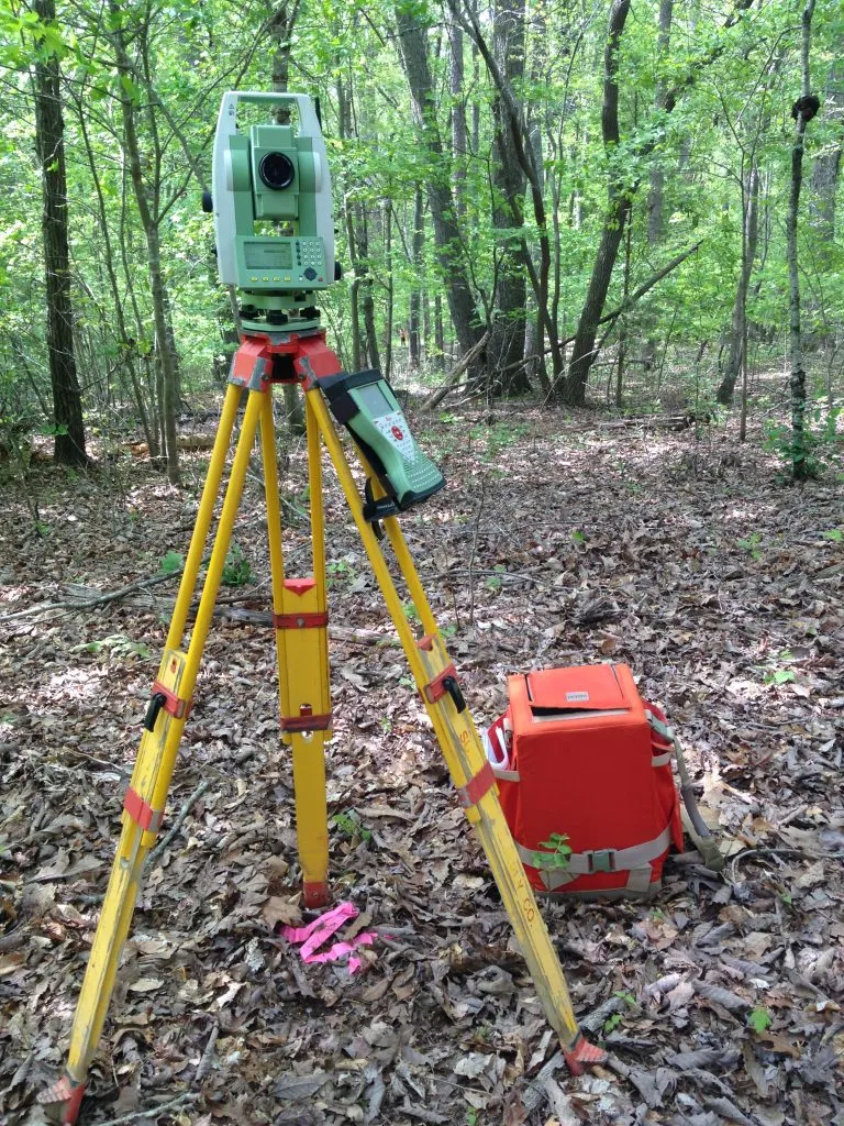 A professional conducting residential land surveying in a forested area of Raleigh.