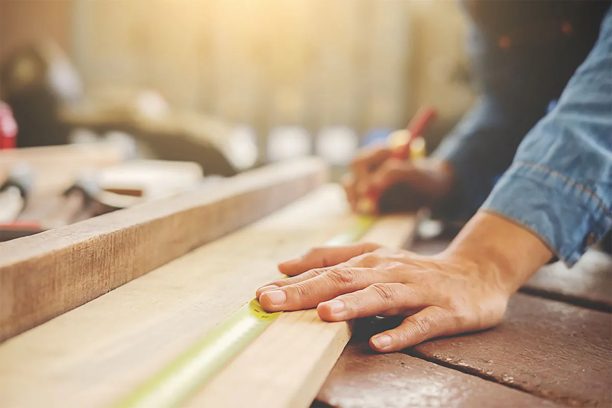 A professional home contractor measuring wood for carpentry project.