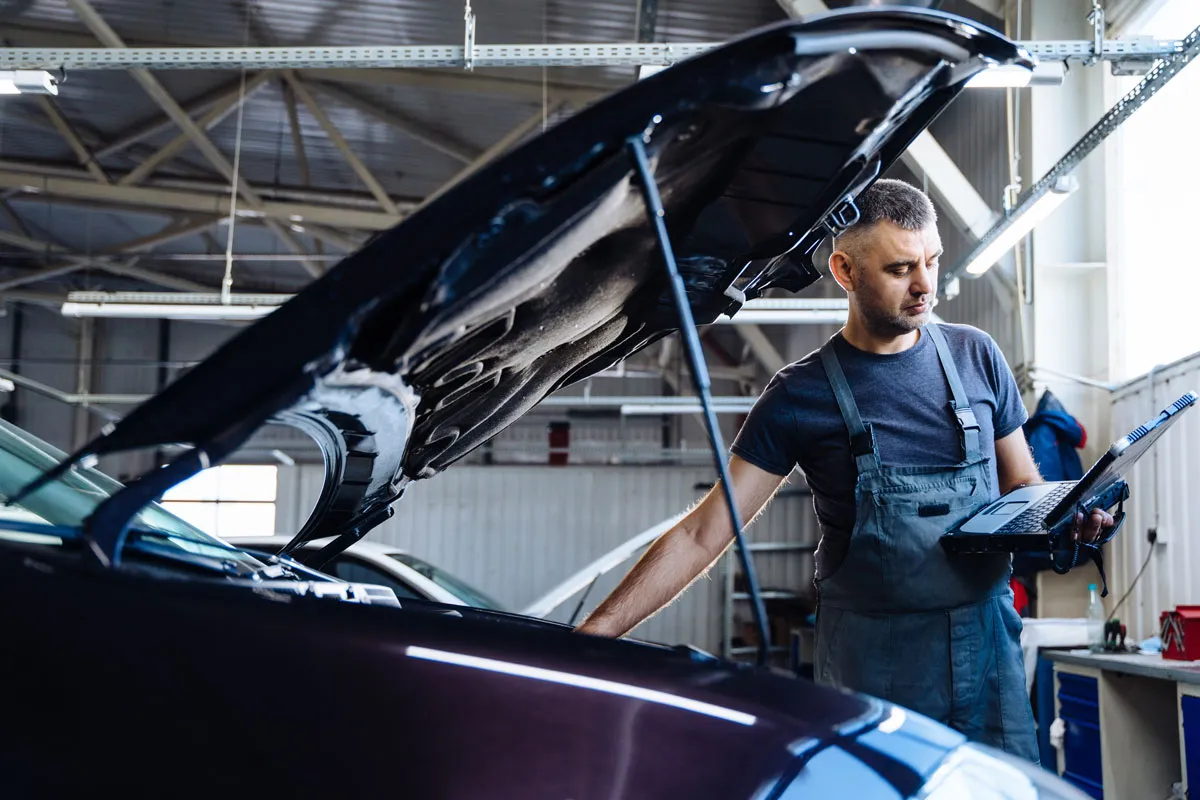A mechanic is providing a helpful service by checking a laptop for diagnostics.