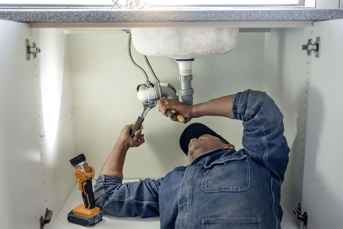 Plumber fixing pipes under a sink.