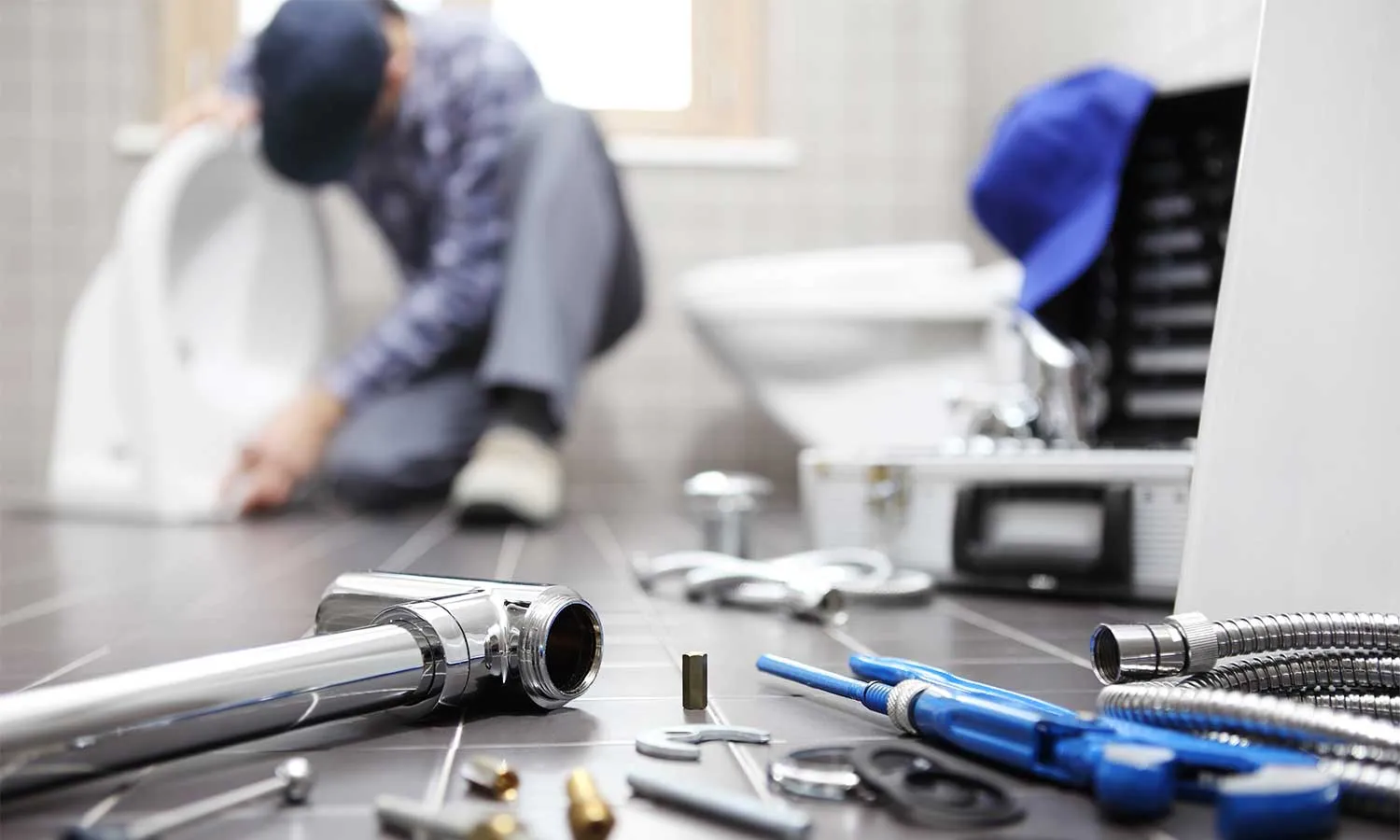 Plumbing tools in the foreground with a plumber in the background providing plumbing repairs in a bathroom.