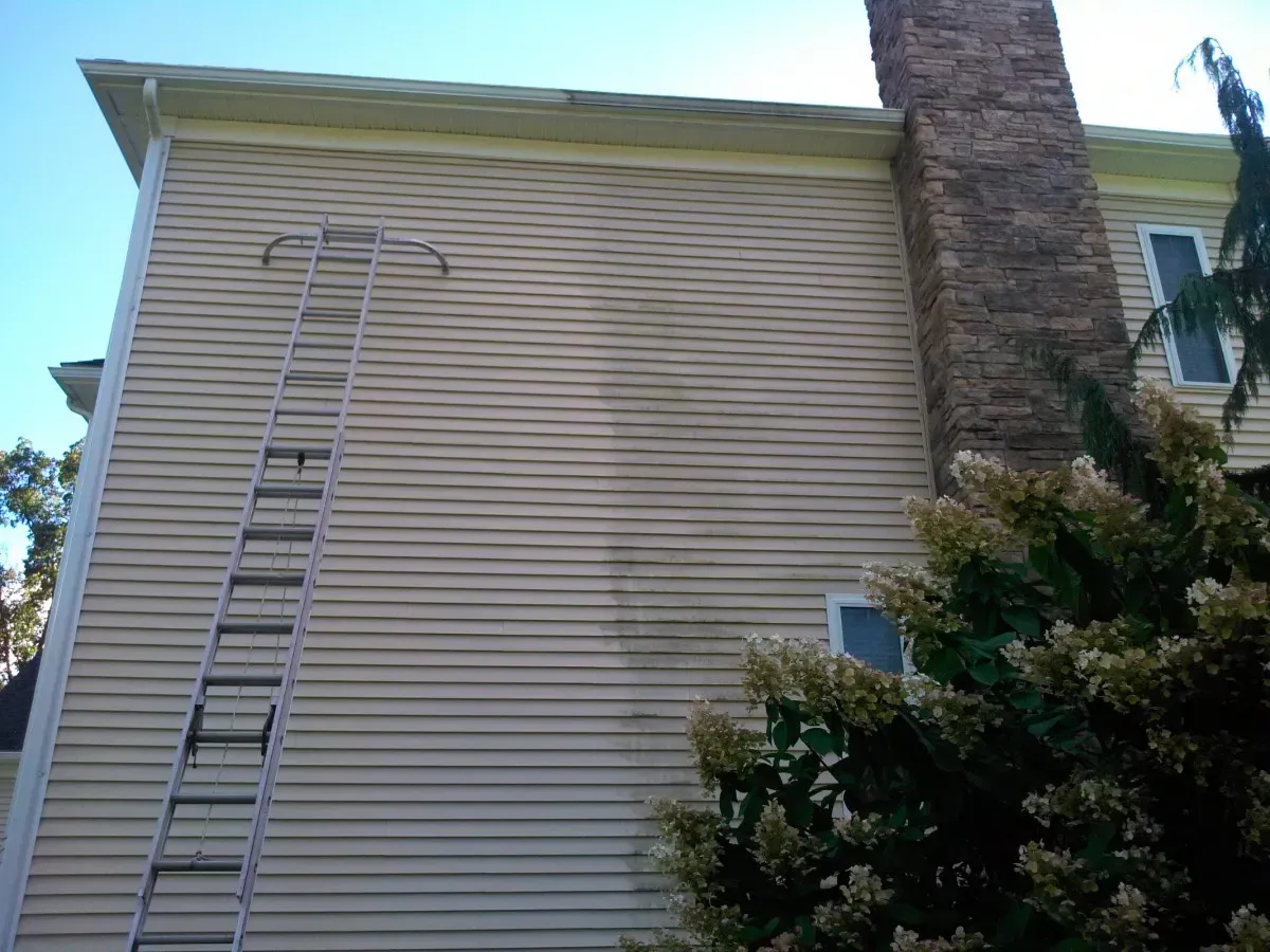 Technician pressure washing the exterior siding of a residential home in Methuen, removing dirt and mildew with professional equipment.