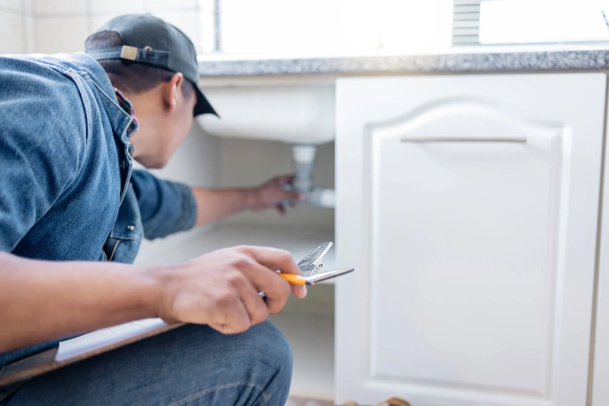 A professional plumbing technician fixing pipe under sink.